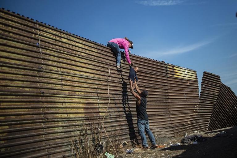 Migranti scavalcano la barriera al confine tra Messico e Stati Uniti vicino a Tijuana, il 25 novembre 2018 (PEDRO PARDO/AFP/Getty Images).