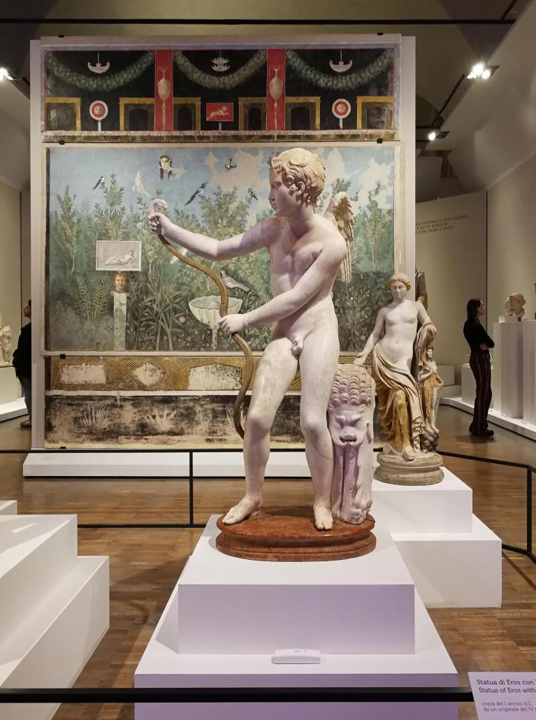 Veduta della seconda sala con Statua di Eros con l’arco (copia del I secolo d.C. da un originale del IV secolo a.C., Venezia, Museo Archeologico Nazionale) in primo piano e in secondo piano Affresco con pittura di giardino (fine I secolo a.C. – prima metà I secolo d.C. Pompei, Parco Archeologico).
