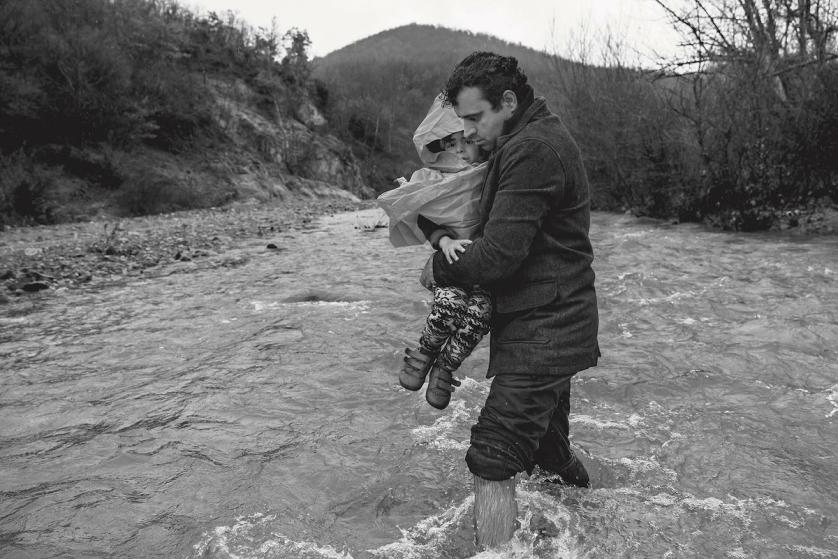 James Nachtwey, Un uomo porta in braccio il figlio mentre tenta di attraversare il confine con la Macedonia. Macedonia, 2016, © James Nachtwey/Contrasto.